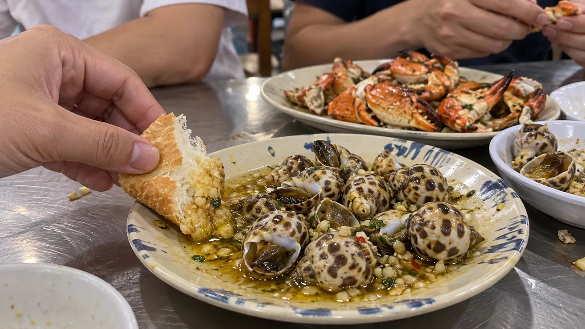 サイゴンの貝料理を分け合い、パンにニンニク風味のソースを染み込ませるイメージ(Ốc Đàoの実際の料理・店内の写真ではありません)
